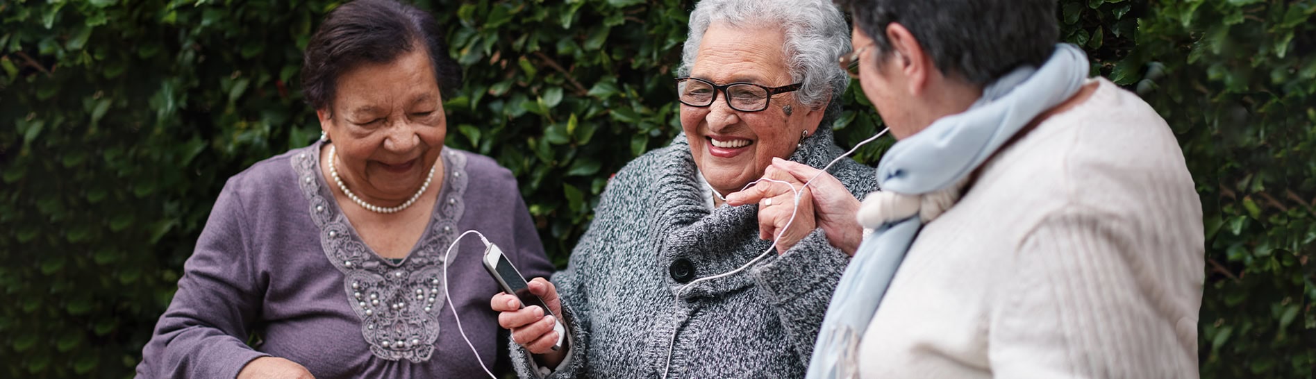 Three women listen to music on a mobile phone and smile at each other