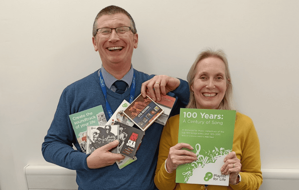 Two people holding Playlist for Life Help Point materials and smiling